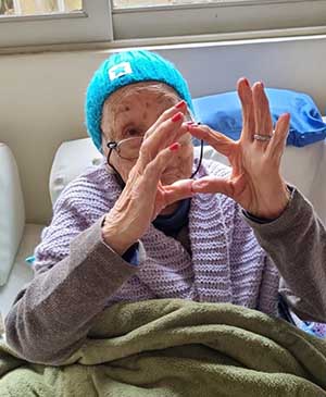 imagem de uma senhora fazendo sinal de coração com as mãos com o gorro azul claro na casa de repouso mamma mia imagem de uma senhora fazendo sinal de coração com as mãos com o gorro azul claro na casa de repouso mamma mia