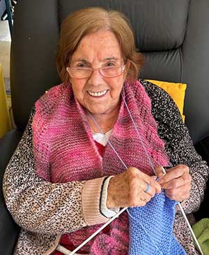 imagem de uma senhora no sofá tricotando uma roupa azul na casa de repouso mamma mia imagem de uma senhora no sofá tricotando uma roupa azul na casa de repouso mamma mia